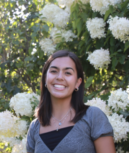 A woman smiling with white flowers behind her. 